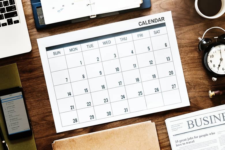 Desk calendar planner with laptop, clock and coffee cup.