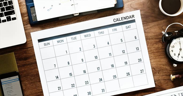 Desk calendar planner with laptop, clock and coffee cup.