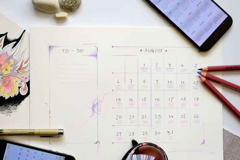 Calendar of August on desk with coloured pencils and mobile phone.