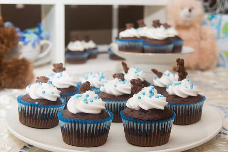 Baby shower cupcakes with teddy bear in the distance.