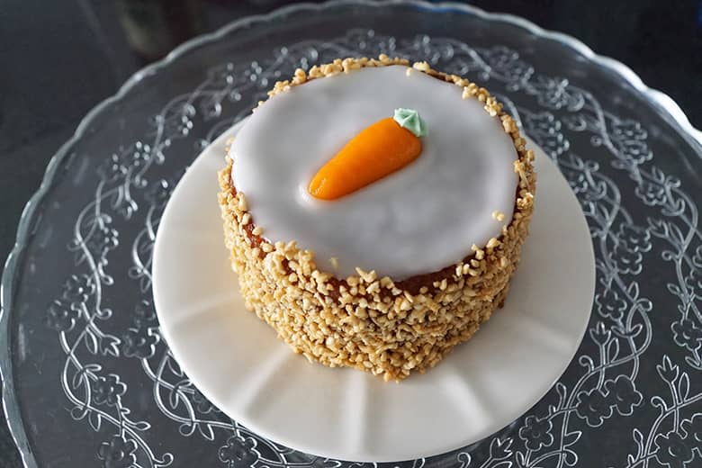 Carrot cake with icing and nuts on a white plate.