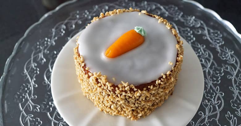 Carrot cake with icing and nuts on a white plate.