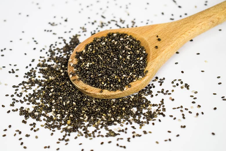 Chia seeds on a wooden spoon spilling over.