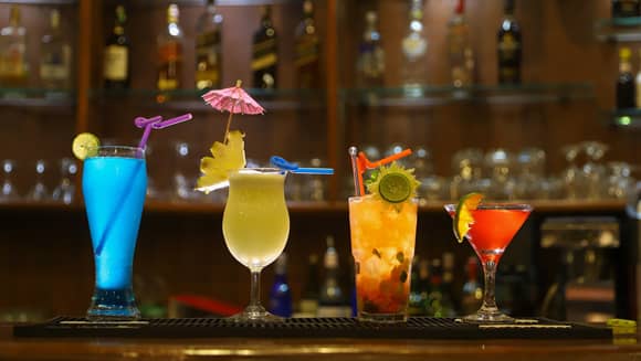 Four different coloured cocktails on a bar.