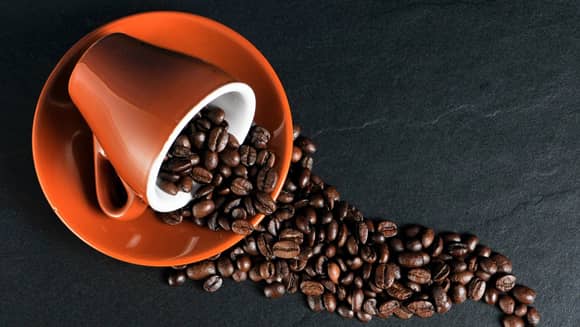 Orange coffee cup on side with coffee beans.