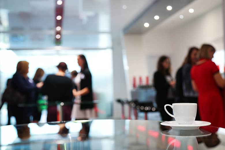 A coffee cup on a table with conference guests in the distance.