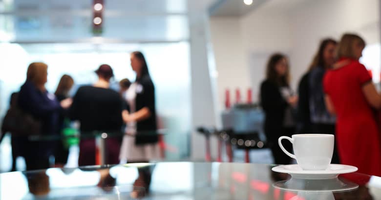 A coffee cup on a table with conference guests in the distance.