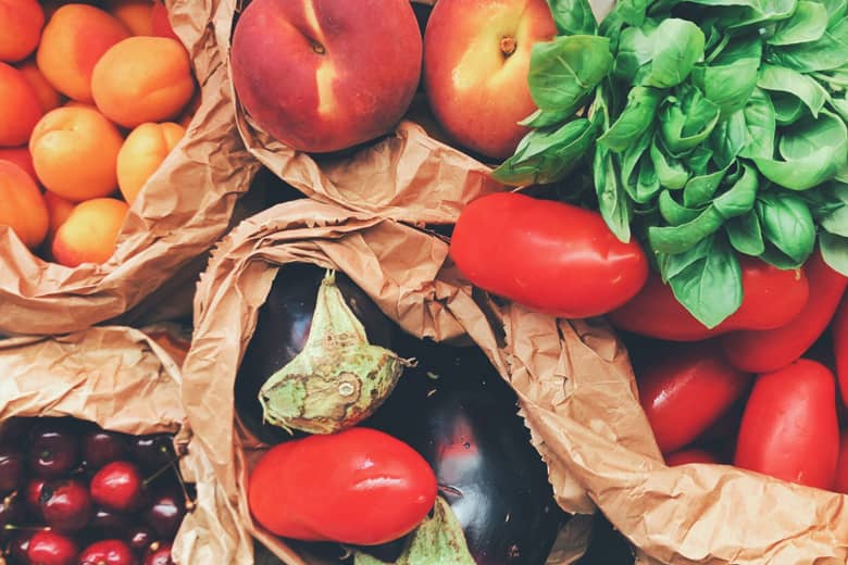 A selection of fresh fruit, vegetables, and herbs in paper bags.