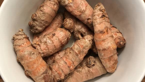 A white bowl of fresh turmeric root.