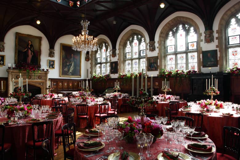 Venue setup for a gala dinner with stained glass windows, tables, place settings and candles.