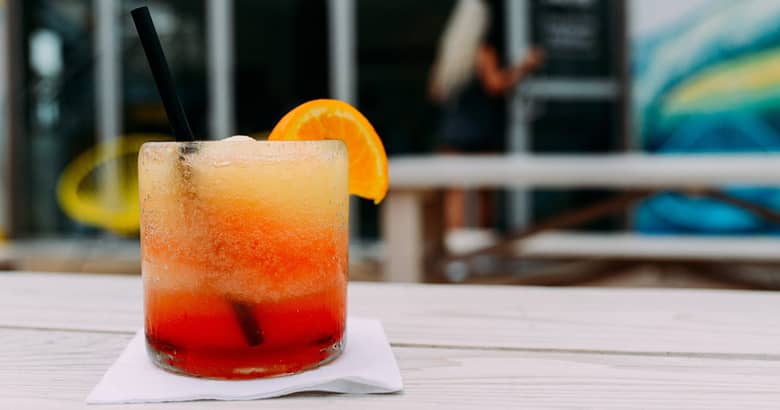 Red and orange mocktail in a glass with orange slice.