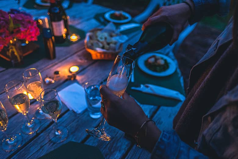 A woman pouring a glass of champagne at an evening outdoor party.