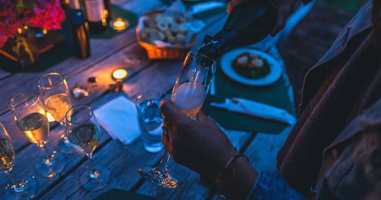A woman pouring a glass of champagne at an evening outdoor party.