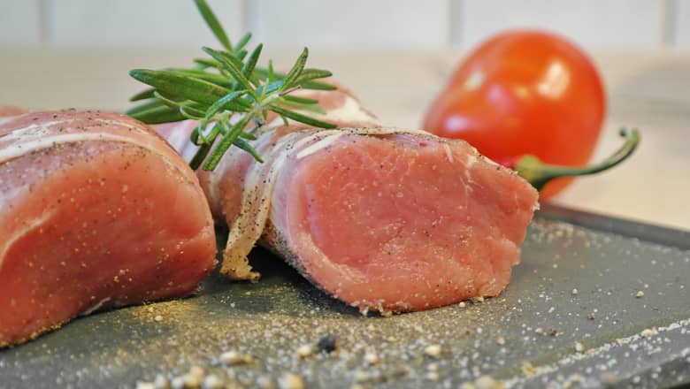 Raw Pork Tenderloin on a board with herbs.