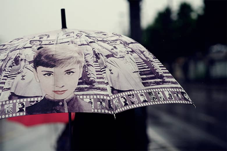 Person walking in the rain with Audrey Hepburn umbrella.