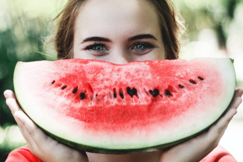 Woman smiling behind a watermelon.