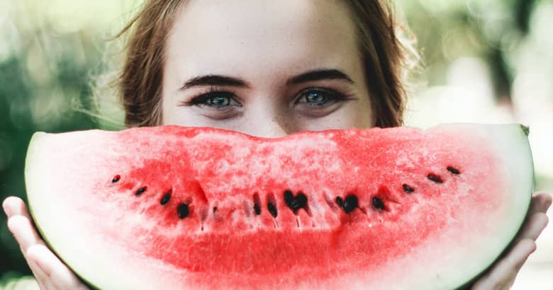 Woman smiling behind a watermelon.