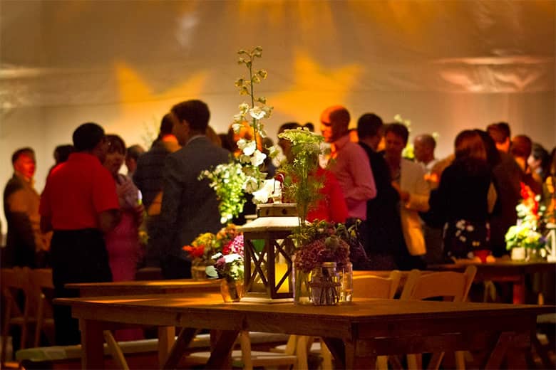 Rustic table with wild flower decorations and lantern with guests mingling behind in the marquee.
