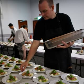 Chef plating up confit salmon with micro watercress and rocket leaf.
