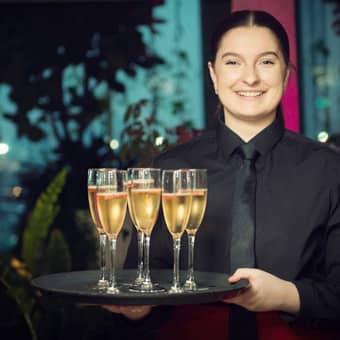 Smiling PenniBlack waitress with a tray of Champagne glasses.