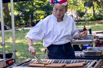 Chef cooking hot dogs on the grill.