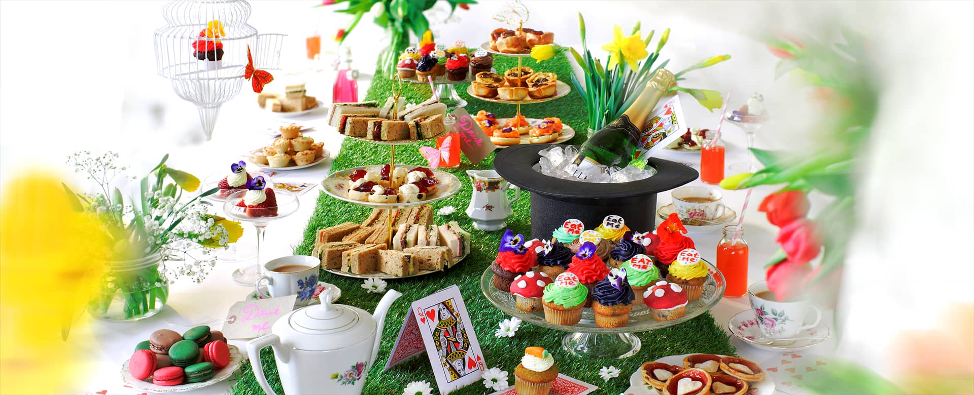 Alice in Wonderland Themed Afternoon Tea with classic cups, teapot, top hat, cards, sandwiches, sweet cakes and macaroons.