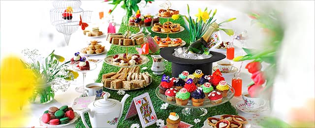 Alice in Wonderland Themed Afternoon Tea with classic cups, teapot, top hat, cards, sandwiches, sweet cakes and macaroons.