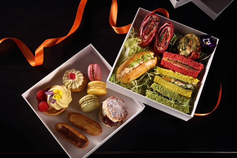 Afternoon tea box containing sandwhiches, quiche, scone, and other treats.