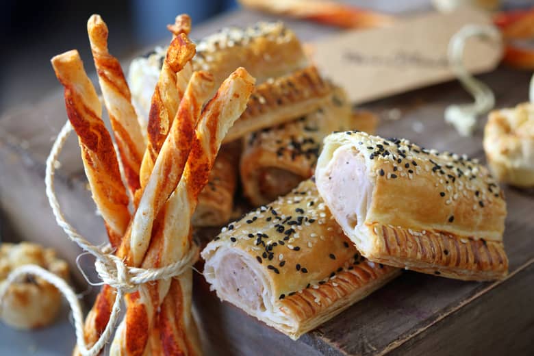Cheese straws with sausage rolls on a rustic board.