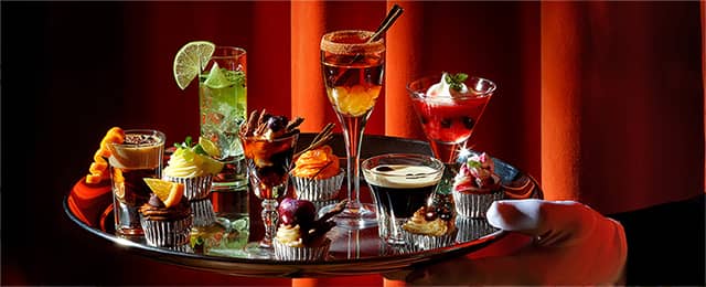 Waiter holding a silver tray containing a range of cakes and cocktails.